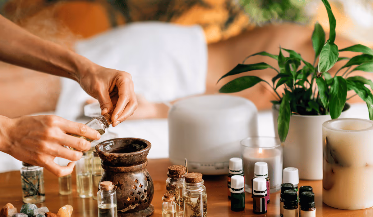 Bottles of aromatherapy oils for relaxation beside a diffuser, oil burner and candle on a wooden table at home