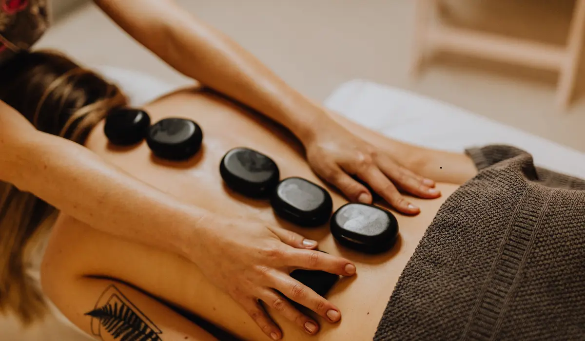 A warm hot-stone back massage in soft lamplight, a therapist's hands resting on a client's back lined with smooth basalt stones
