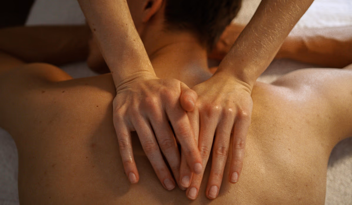 Close-up of a therapist's crossed hands massaging bare, oiled shoulders, illustrating how often you should get a massage for ongoing relief