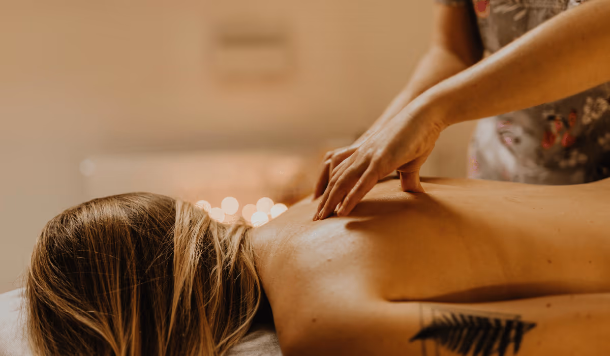 A therapist's hands working the upper back and shoulders of a woman lying face down in warm candlelight, during a massage for stress relief